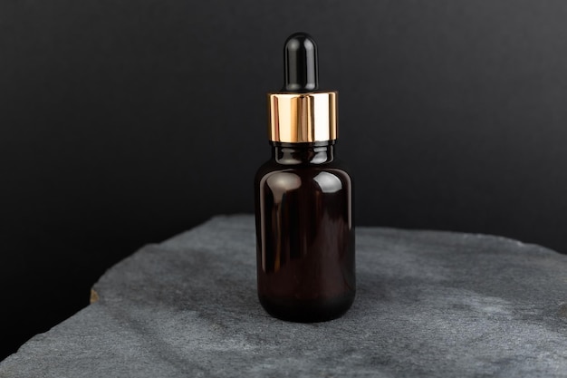 Flacon marron avec compte-gouttes avec un sérum de beauté sur une pierre de granit sur fond noir Emballage en verre pour produit cosmétique huile essentielle d'arôme Soins de la peau hydratation et nutrition au collagène