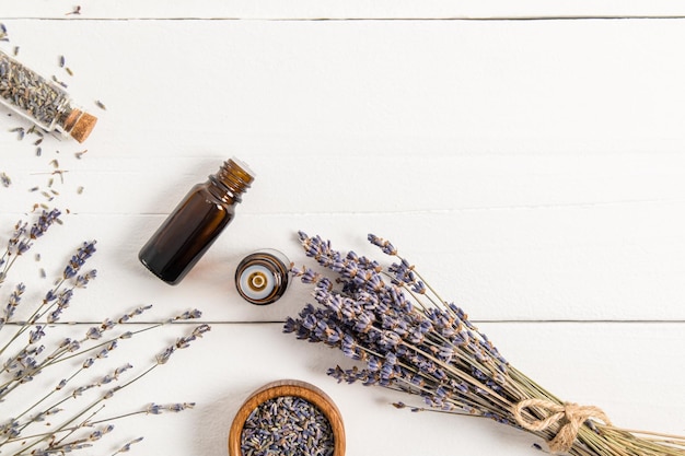 Flacon médical ouvert avec un compte-gouttes à l'huile de lavande naturelle biologique et sur un fond en bois blanc avec un bouquet de lavande sèche