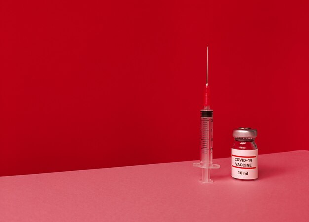 Flacon médical avec vaccin covid 19 et seringue sur fond rouge avec skyline tendance inclinée et espace de copie.