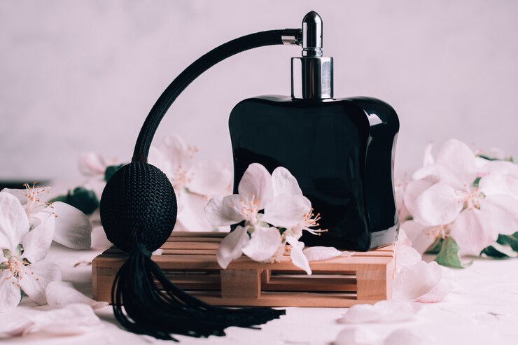 Flacon noir eau de toilette ou parfum avec longue pompe à pompon, sur podium en bois en forme de palette sur une surface en plâtre clair avec des fleurs de pomme