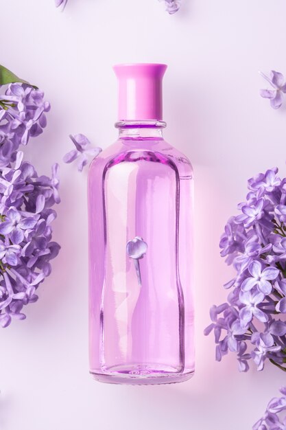 Flacon de parfum avec des fleurs lilas sur mur blanc