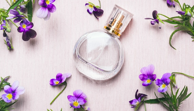 Flacon de parfum pour femme et fleurs violettes sur fond rose