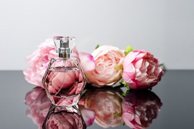 Flacon de parfum rose avec des fleurs sur une surface en noir et blanc