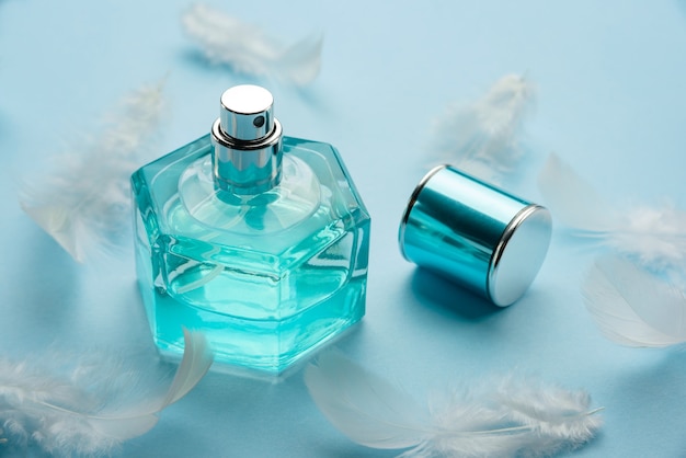 Flacon De Parfum Sur Une Surface Bleue Avec Des Plumes Blanches.