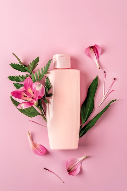 Flacon rose avec crème hydratante sur fond rose avec fleurs Alstroemeria. Maquette de conteneur cosmétique avec place pour le texte. Concept de produit de beauté de soins de la peau naturels.