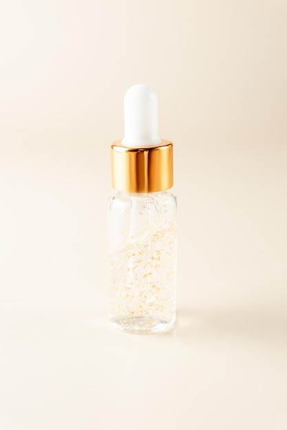 Flacon transparent avec sérum de beauté, acide hyaluronique, or 24 carats et vitamines sur fond beige. Concept de traitement de soins du visage et du corps à domicile de luxe.