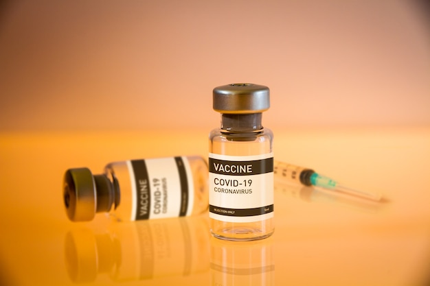 Flacon de vaccin Covid-19 et seringue sur un fond de laboratoire jaune