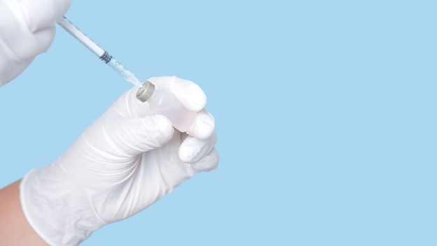 Flacon de vaccin et seringue à la main portant des gants en caoutchouc blanc isolés sur fond bleu.