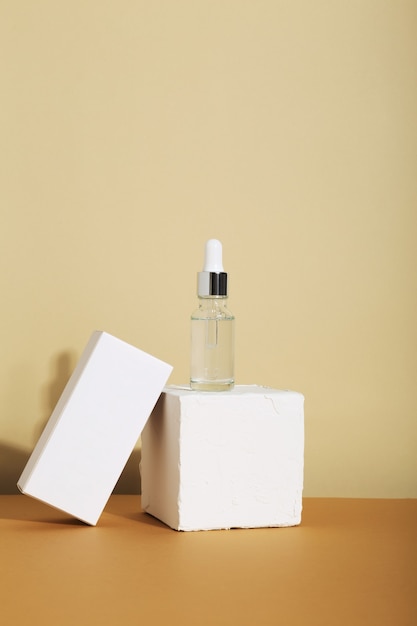 Flacon en verre blanc avec compte-gouttes sur fond beige et boite blanche. Produit cosmétique naturel pour le concept de soins de la peau