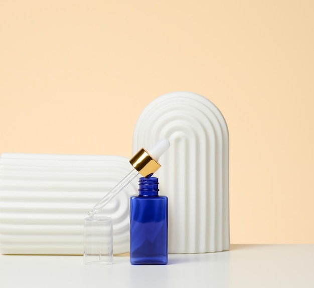 Le flacon en verre bleu avec pipette se dresse sur fond beige. Marque de SPA de cosmétiques. Emballage pour gel, sérum, publicité et promotion de produits, maquette