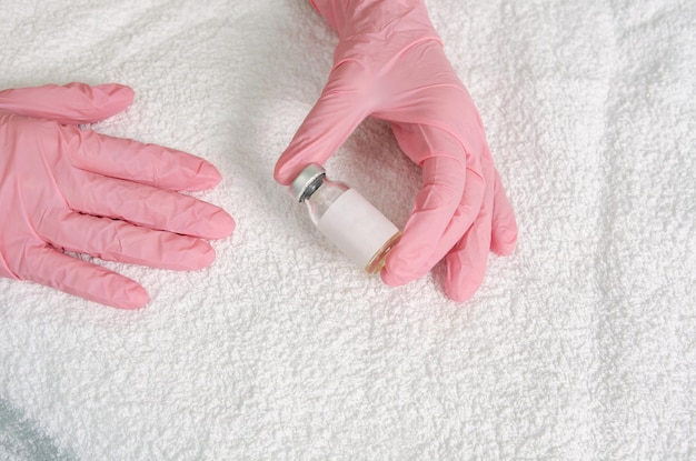 Flacon en verre de vaccin à la main dans des gants médicaux sur fond de tissu blanc