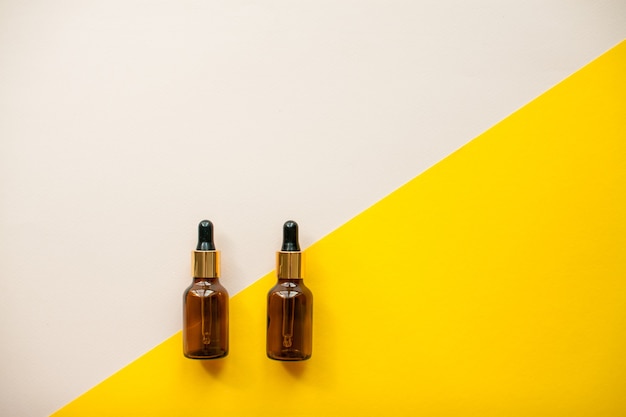 Flacons cosmétiques pour huile de sérum ou crème sur fond jaune vif et rose clair