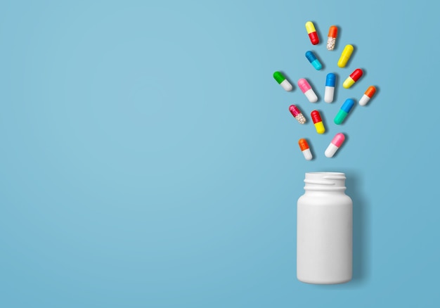 Flacons de médicaments blancs, pilules jaunes, comprimés gris, pilules blanches et pilules rouges sur fond bleu,