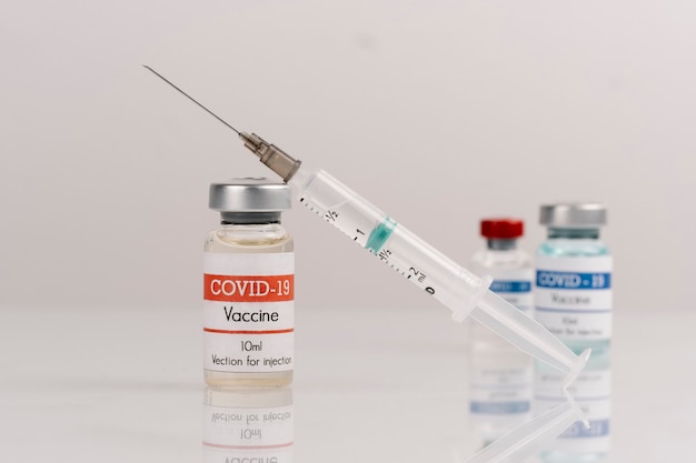 Flacons de vaccin Covid-19 avec seringue sur une surface blanche