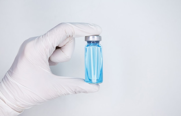 Flacons en verre bleu pour échantillons liquides tenus par une main avec des gants médicaux blancs sur fond blanc