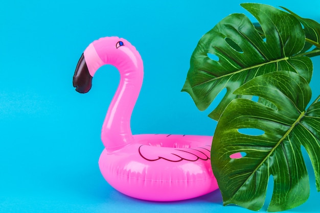 Flamant rose gonflable sur fond bleu avec des feuilles de monstera.