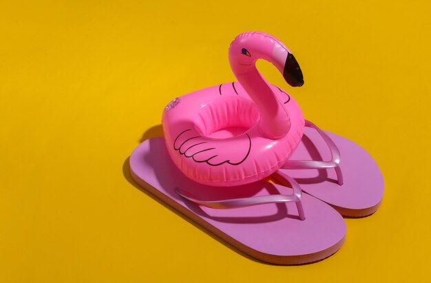 Flamant rose gonflable avec des tongs sur fond jaune ensoleillé. Été, concept de vacances à la plage. Minimalisme.