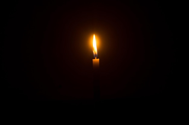 Flamme de bougie allumée unique ou lumière rougeoyante sur une bougie orange sur fond noir ou sombre sur la table de l'église pour les funérailles de Noël ou le service commémoratif