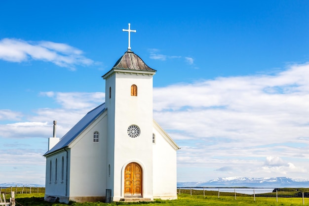 Flateyjarkirkja église luthérienne blanche avec prairie en premier plan et fjord de la mer avec ciel bleu et montagnes en arrière-plan île de Flatey Islande