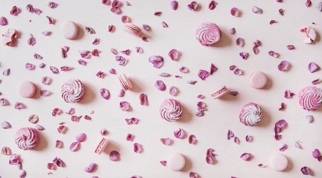 Flatlay de biscuits macaron guimauves et pétales sur fond rose