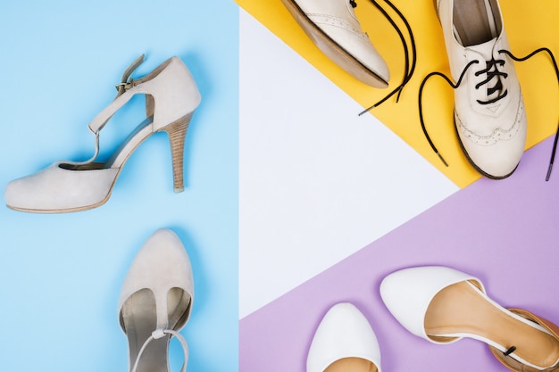 Flatlay élégant avec diverses chaussures à la mode féminines: chaussures brogues, appartements, chaussures à talons hauts sur fond bleu, violet, blanc et jaune. Copyspace