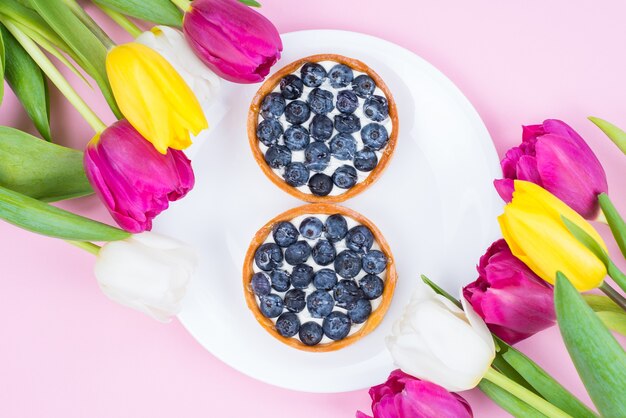 Flatlay flatlay top au-dessus de la photo en gros de beau dessert délicieux savoureux sur plaque avec cadre de fleur isolé surface de couleur pastel