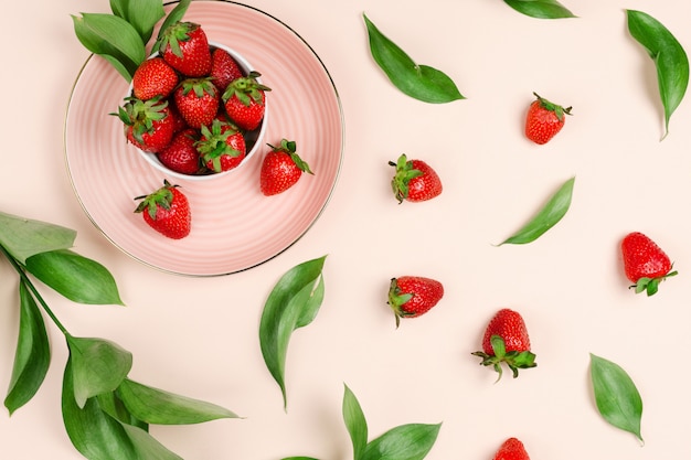 Flatlay avec des fraises biologiques fraîches dans une assiette avec des feuilles de ruscus et des branches autour