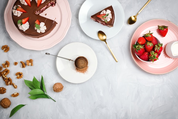 Flatlay avec gâteau au chocolat végétalien, fraises, noix, cacao et autres ingrédients de dessert sur fond de ciment avec fond