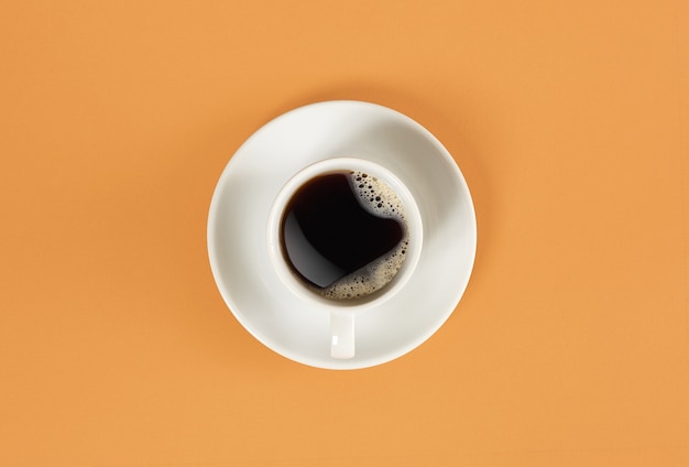 Flèches d'une horloge dans une tasse de café sur fond orange vue d'en haut