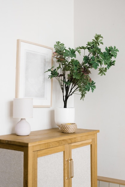 Une fleur artificielle dans un pot sur une commode en bois dans les objets de décoration du salon et un cadre au mur dans un style minimaliste scandinave