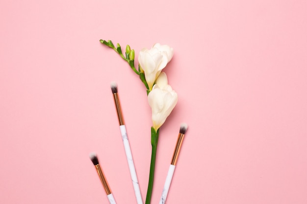 Fleur blanche avec des pinceaux à maquillage sur fond rose