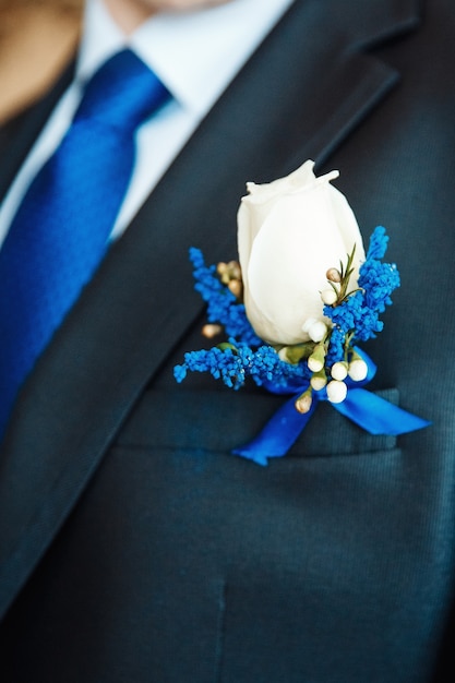 Fleur de boutonnière de delphinium rose blanche et bleue sur le manteau de mariage du marié avec une cravate bleue