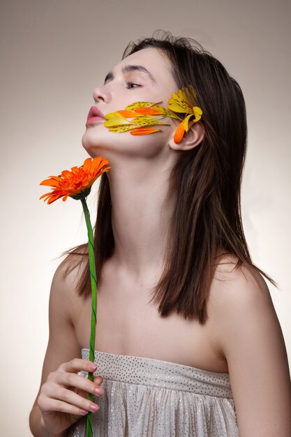 Fleur dans les mains. Modèle attrayant maigre avec des cheveux raides foncés posant avec une fleur dans les mains