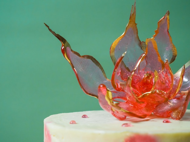 Une fleur d'isomalt rouge comestible sur un gâteau sur fond vert pâle