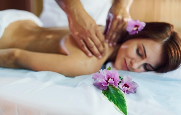 Fleur pourpre allongée L'homme fait un massage à la jeune femme dans une serviette blanche à l'intérieur