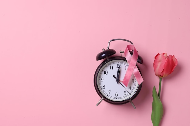 Fleur, réveil et ruban rose sur fond rose. Sensibilisation au cancer du sein d'octobre.