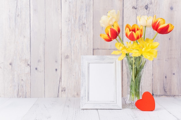 Fleur de tulipe dans un vase en verre avec décor de cadre photo sur un mur de fond de table en bois à la maison, gros plan, concept de design pour la fête des mères.