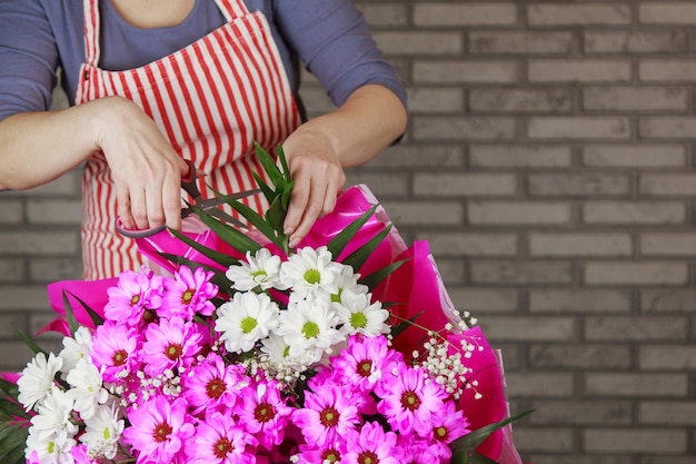 Photo une fleuriste attache un noeud de ruban sur un bouquet de fleurs enveloppées dans du papier kraft sur le dessus du bureau