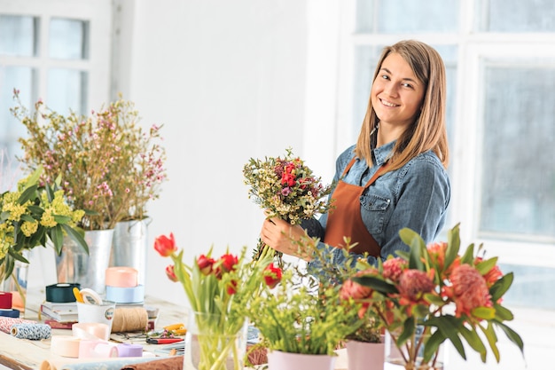 Fleuriste au travail : la jeune fille faisant le bouquet moderne de mode de différentes fleurs