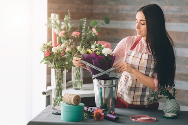 Fleuriste au travail: jolie jeune femme brune faisant de la mode un bouquet moderne de fleurs différentes. Femmes travaillant avec des fleurs en atelier