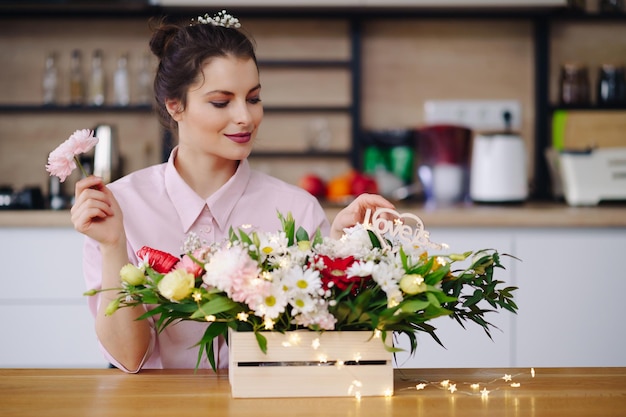 Fleuriste au travail jolie jeune femme brune faisant de la mode composition moderne de différentes fleurs décorant avec des lumières led à la maison