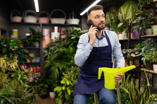 Fleuriste dans la jardinerie arrosant et prenant soin des plantes en pot en parlant au téléphone