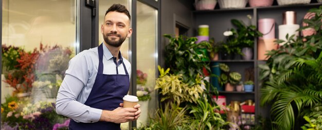 Un fleuriste dans un magasin de fleurs se tient à côté d'un réfrigérateur avec un verre de café dans les mains