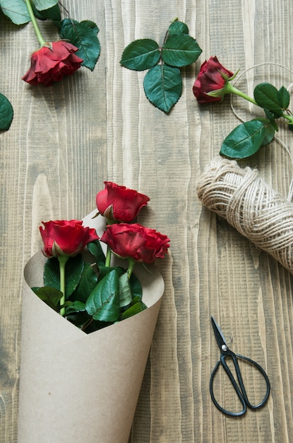 Fleuriste faisant un bouquet de roses rouges, enveloppé dans du papier kraft sur une table en bois