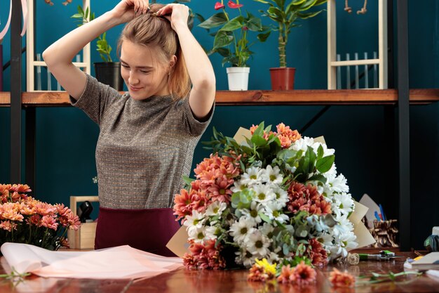 Photo le fleuriste fait un bouquet de chrysanthèmes. une jeune fille adulte redresse ses cheveux sur sa tête.