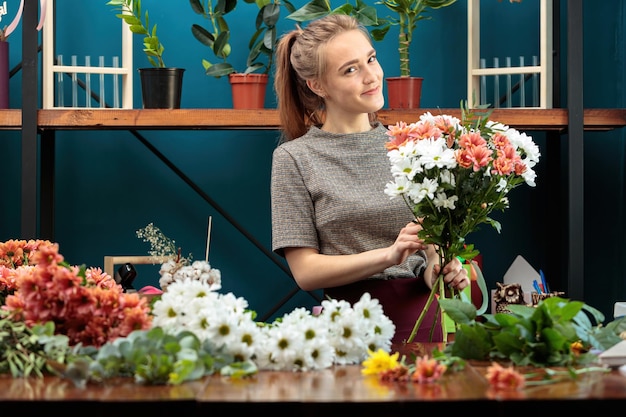 Fleuriste fait un bouquet de chrysanthèmes multicolores Une jeune fille adulte regarde la caméra et sourit