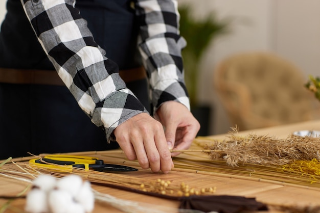 Le fleuriste fait des compositions sèches de fleurs séchées sur une table en bois, gros plan