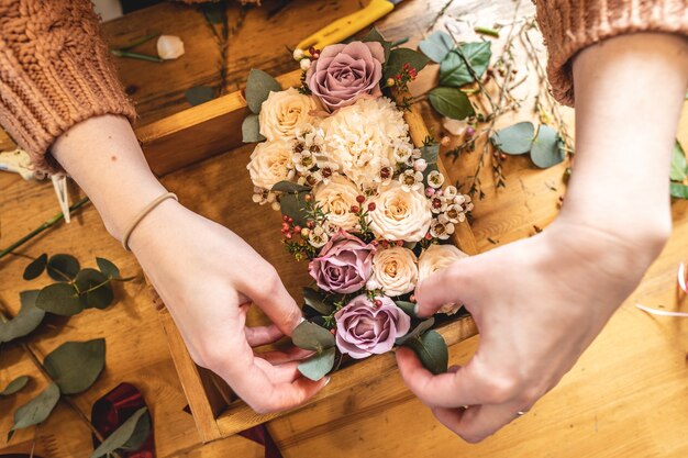 Fleuriste femme recueille une composition de fleurs dans une boîte en bois avec les mains