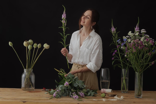 Fleuriste fille recueille un bouquet dans un atelier de fleurs sur un fond sombre mise en page pour la fleuristerie