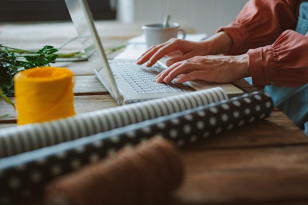 Fleuriste hipster fille élégante à la mode dans un tablier de travail ordinateur portable de travail regardant un smartphone